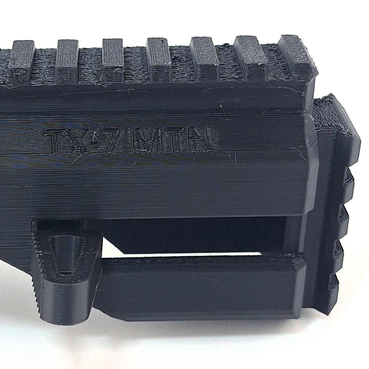 Close-up image of black TX22 MTN Chassis modular firearm component with textured surface and engraved branding